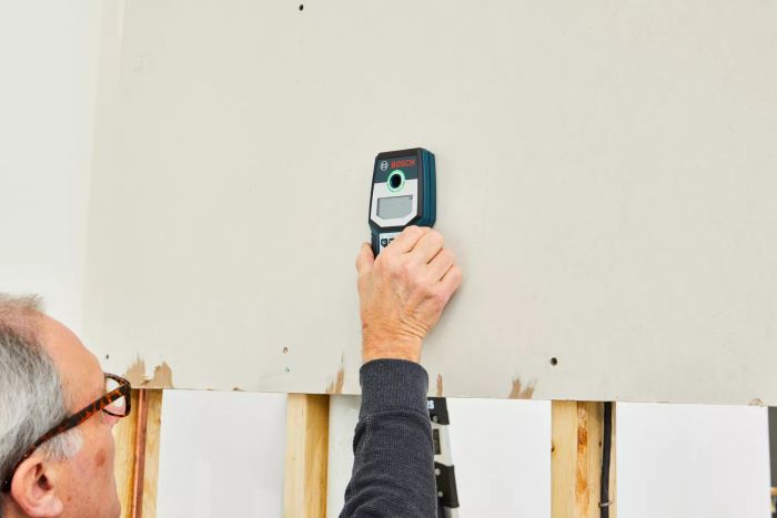 A person using the Bosch GMS120 Digital Multi-Scanner to detect objects behind walls
