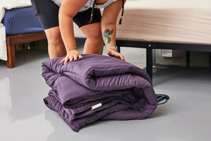 A person folding the Utopia Bedding All-Season Down Alternative Comforter beside a neatly made bed
