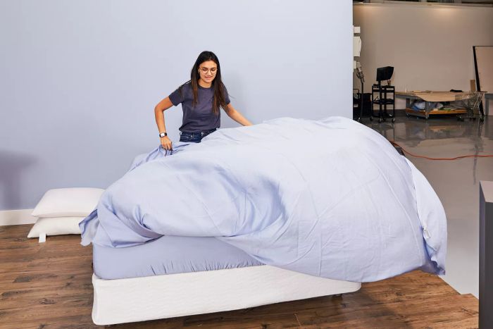 A person laying out the Sijo AiryWeight Eucalyptus Sheet Set on a bed