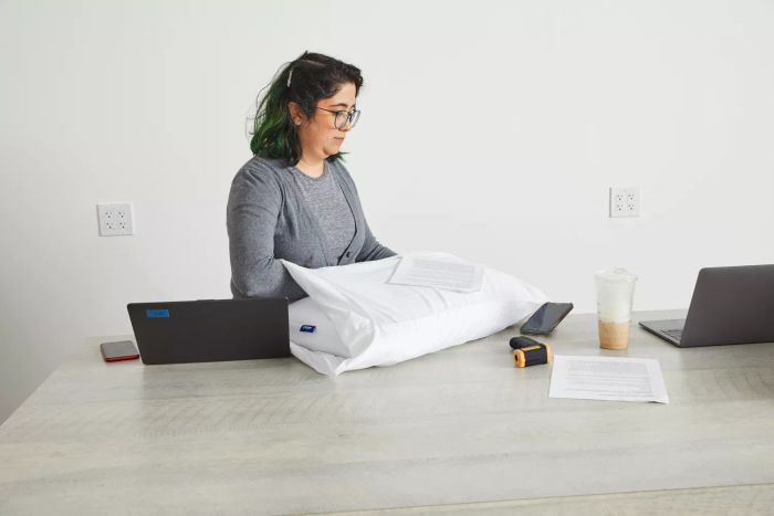 A woman holding the Casper Foam Pillow with Snow Technology on a table alongside laptops.