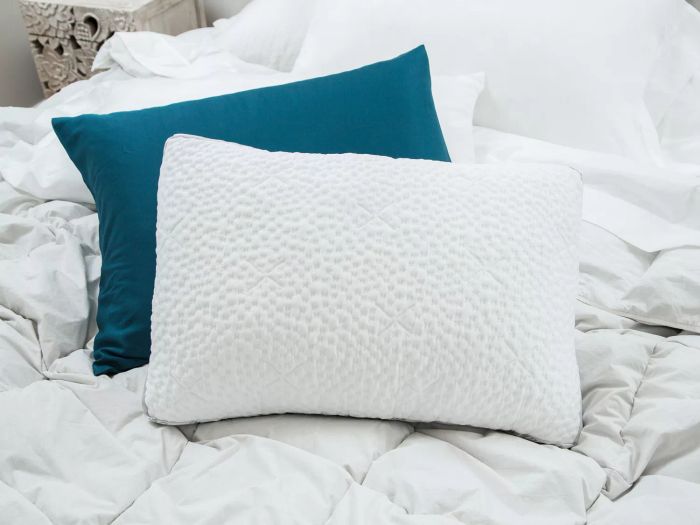 The Nest Bedding Easy Breather Natural Pillow is showcased on a bed, with a nearby pillow neatly covered by a pillowcase.