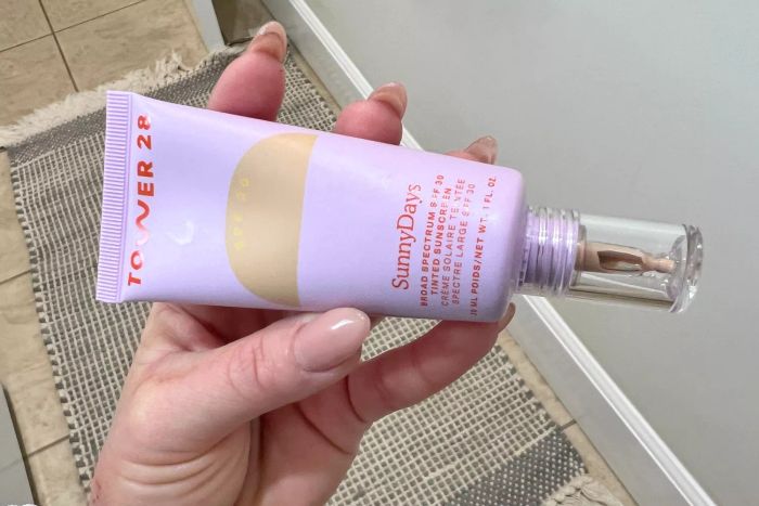 A person holds a tube of Tower 28 SunnyDays SPF 30 Tinted Sunscreen