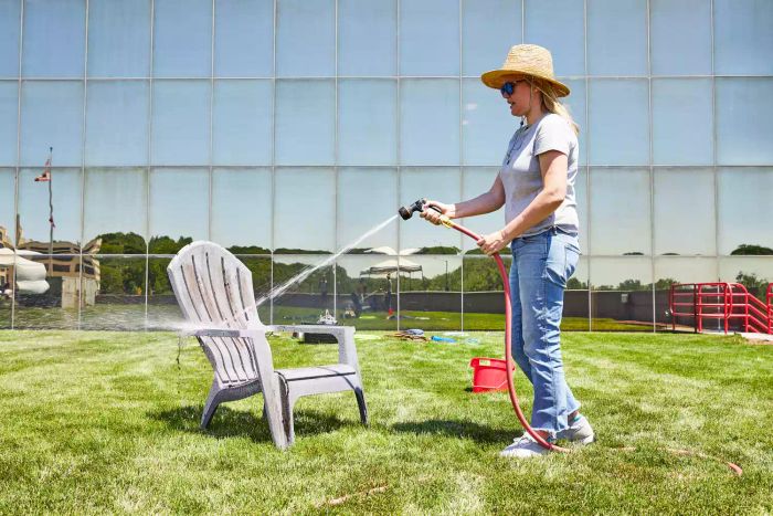 Person using the Melnor Rear Trigger Nozzle to spray water on an Adirondack chair displayed on a grass lawn