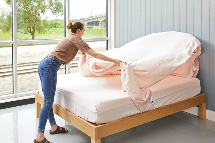 A person spreading a Linenwalas 100% Tencel Lyocell Bed Sheet over a mattress