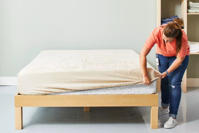 A woman tucking the fitted sheet from the Sheex Arctic Aire Max set onto the corner of a mattress
