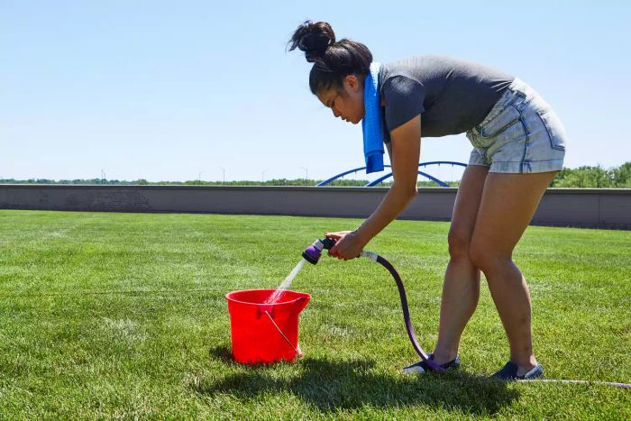 Person filling a red bucket with water using the Dramm Revolution 9-Pattern Spray Gun