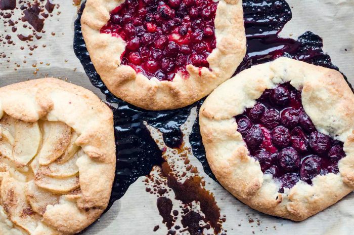 A homemade fruit and berry galette fresh out of the oven. The process of baking. Open pie with apples, cranberries, and cherries. Fruit-based pastry. Summer dessert served on parchment paper.