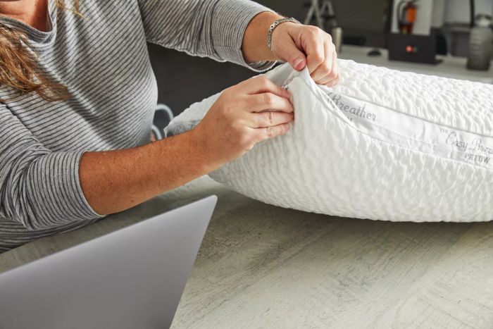 A person is zipping up the Nest Bedding Easy Breather Natural Pillow, which is placed on a table.