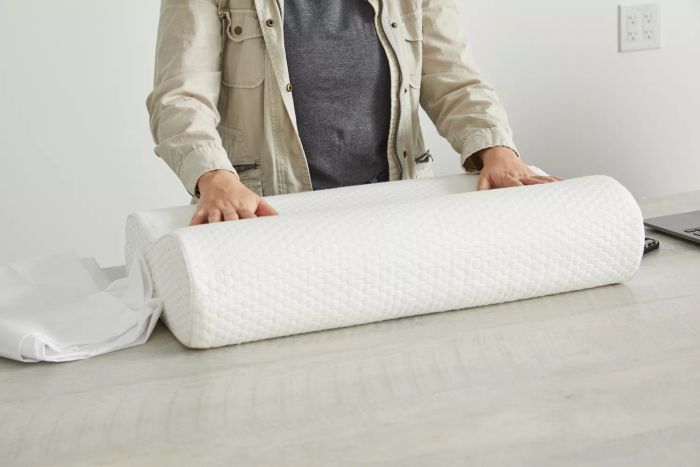 A person is pressing down on a Uttu Sandwich Pillow placed on a table.