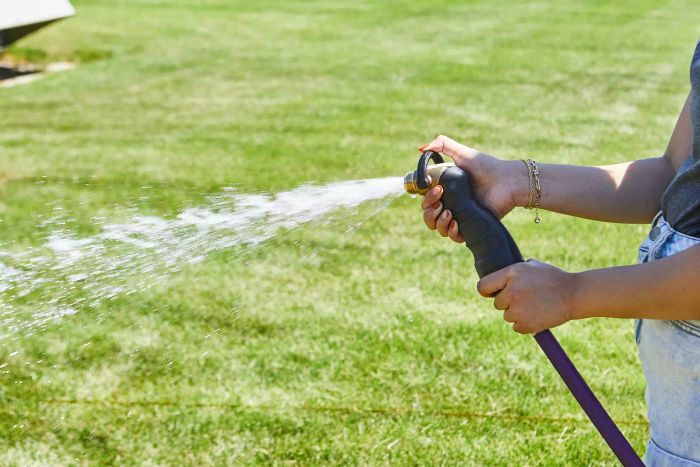 Hands spraying water with the Eley Brass Garden Hose Nozzle across a grass lawn