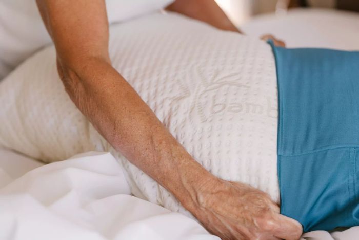 A person is seen placing the Snuggle-Pedic Adjustable Shredded Memory Foam Pillow into a blue pillowcase.