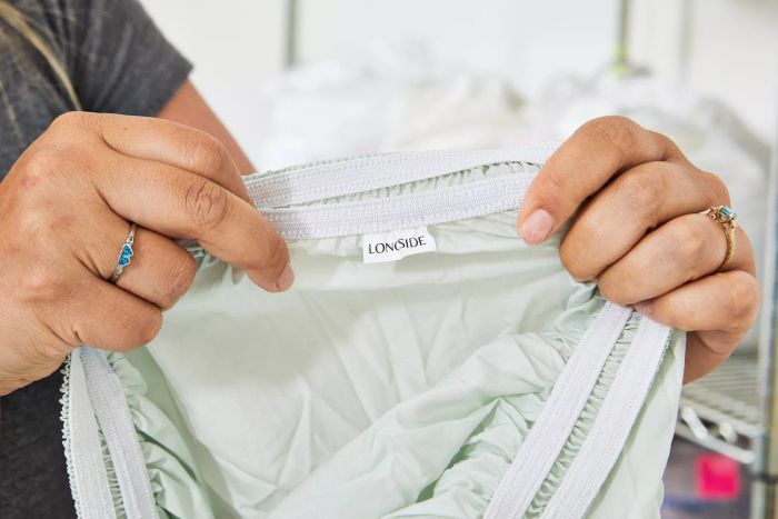 A person holding the Sweave Bedding Eucalyptus Tencel Lyocell Sheets with the logo tag visible