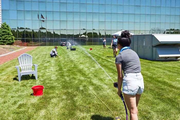 Person spraying water with the Dramm Revolution 9-Pattern Spray Gun with nearby Adirondack chair and red bucket