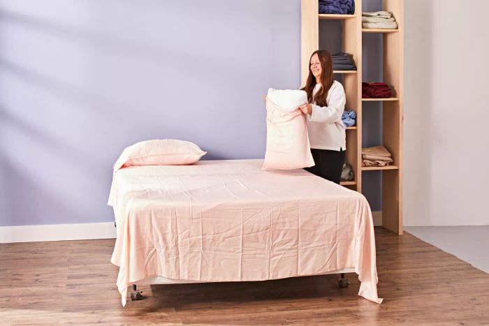 A person placing a pillowcase from the Buffy Breeze Sheet Set onto a pillow on a bed