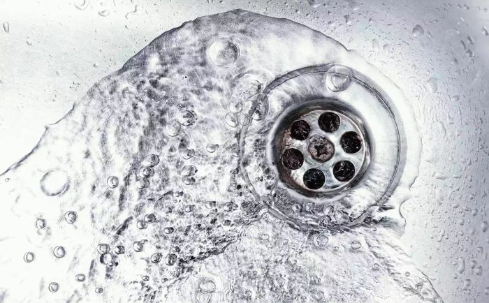 Water flowing down a stainless steel kitchen sink drain. Top view of the washbasin with household plumbing. Cleaning and hygiene concept.