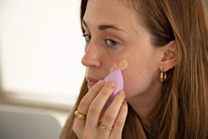 A close-up of a person blending skin tint onto their face using a makeup sponge