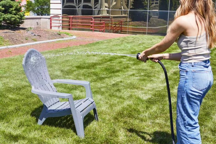 Person using the Frontgate Heavy Duty Spray Hose Nozzle to spray water on an Adirondack chair displayed on a grass lawn