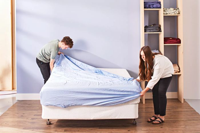 Two individuals placing an Olive + Crate Cooling Eucalyptus Sheet Set onto a mattress
