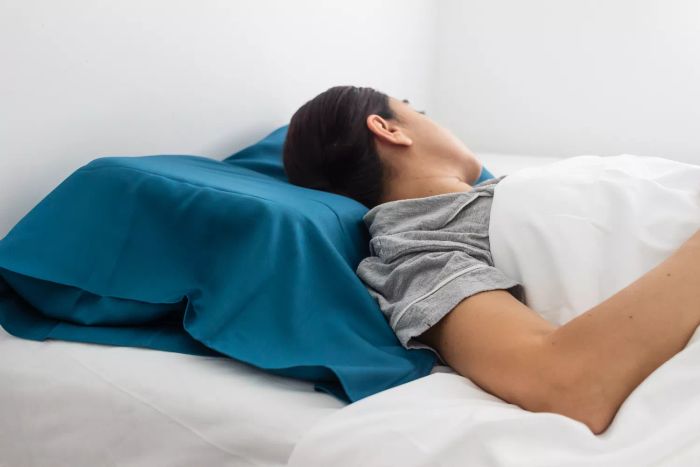 A person is sleeping on their back, using The Company Store Neck Support Memory Foam Pillow.