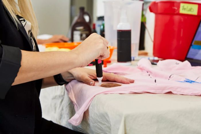 A person applying Tide To Go Instant Stain Remover to a stained T-shirt