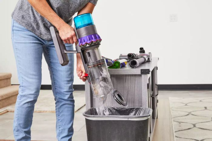 A person empties the canister of a Dyson Gen5detect Cordless HEPA Vacuum into a trash can.