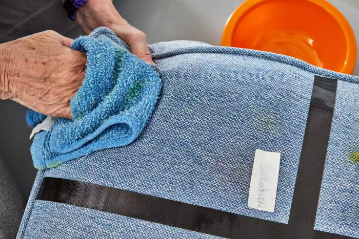 Hands wiping a cushion with a washcloth
