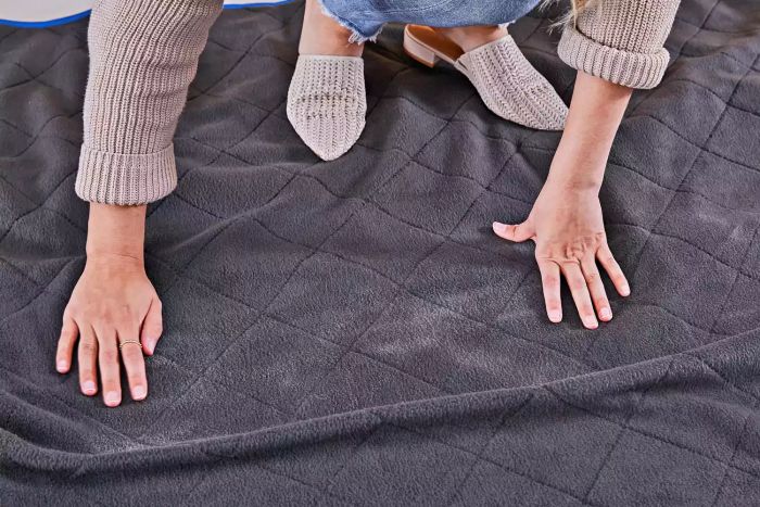 Person standing on the Down Under Outdoors Quilted Fleece Stadium Blanket while adjusting it