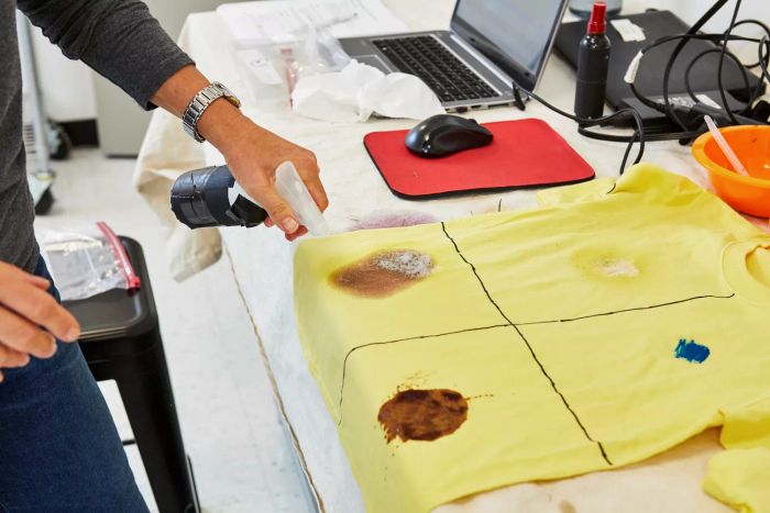 A person applying HEX Performance Stain & Stink Remover to a stained T-shirt
