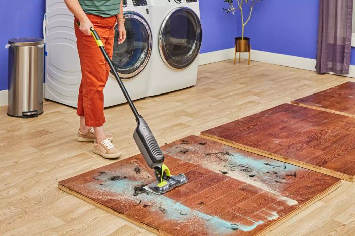 A person is cleaning debris from a wooden floor using the Shark VM252 Vacmop Pro Cordless Wet/Dry Stick Vacuum