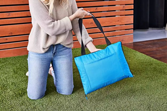 Person kneeling on turf while holding a Roebury Outdoor Picnic Blanket