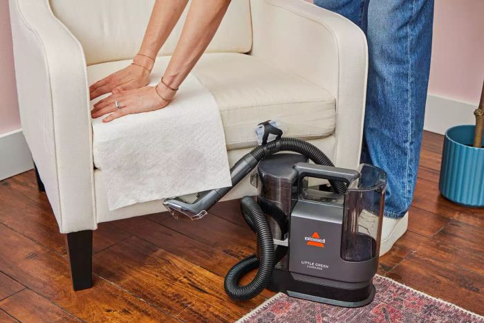 A person drying upholstery after cleaning with the Bissell Little Green Cordless Portable Carpet Cleaner 3682