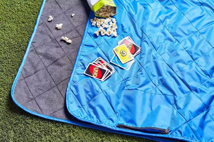 Down Under Outdoors Quilted Fleece Stadium Blanket laid out on grass with popcorn and UNO cards placed on top