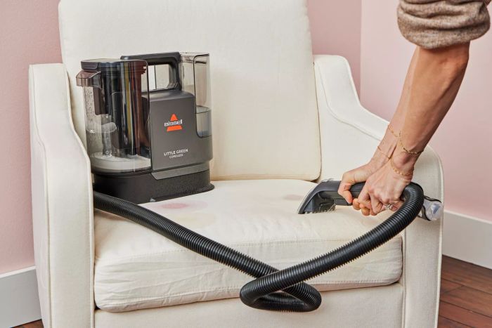 A person cleaning a white chair with the Bissell Little Green Cordless Portable Carpet Cleaner 3682