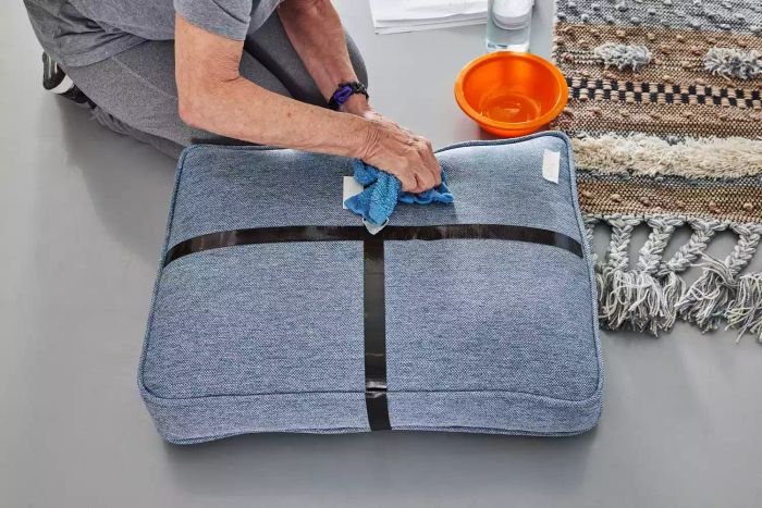 A person wiping a cushion with a washcloth