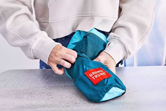 Person packing a folded Grand Trunk Parasheet Picnic Blanket into its storage bag