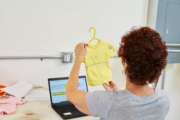 A person examining a T-shirt in front of a laptop