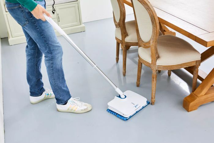 A person mopping under a dining room table using Nellie's Wow Too Bundle