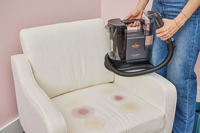 A person cleaning a stained white chair with the Bissell Little Green Cordless Portable Carpet Cleaner 3682