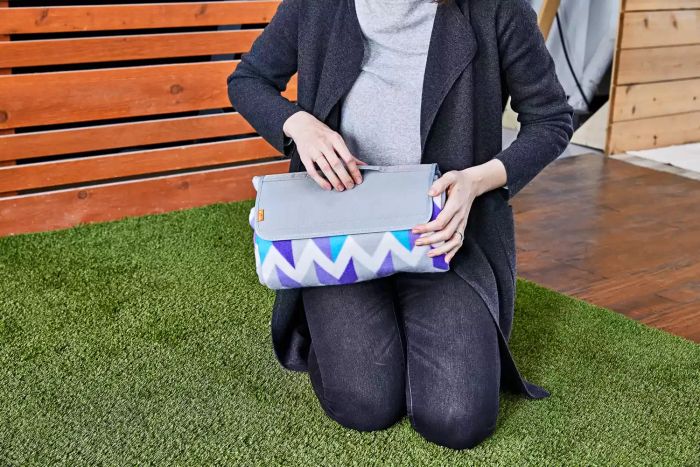 Person holding a neatly folded Yodo Outdoor Picnic Blanket on grass