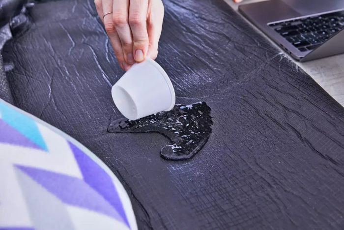 Hand testing the Yodo Outdoor Picnic Blanket by pouring liquid next to a laptop