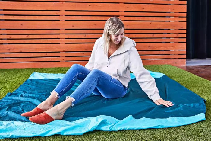 Woman seated on a Grand Trunk Parasheet Picnic Blanket laid out on turf