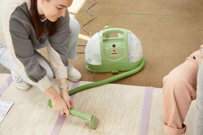 A person cleaning a carpet stain with the Bissell Little Green Cleaner