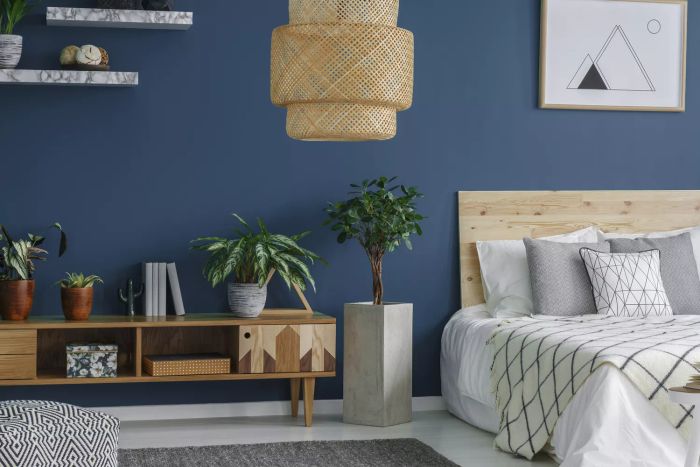 A side view of a blue-themed bedroom featuring a modern lamp, double bed, plants, and a cabinet.