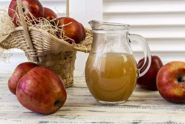 A jug of apple cider placed beside fresh red apples on a rustic wooden table