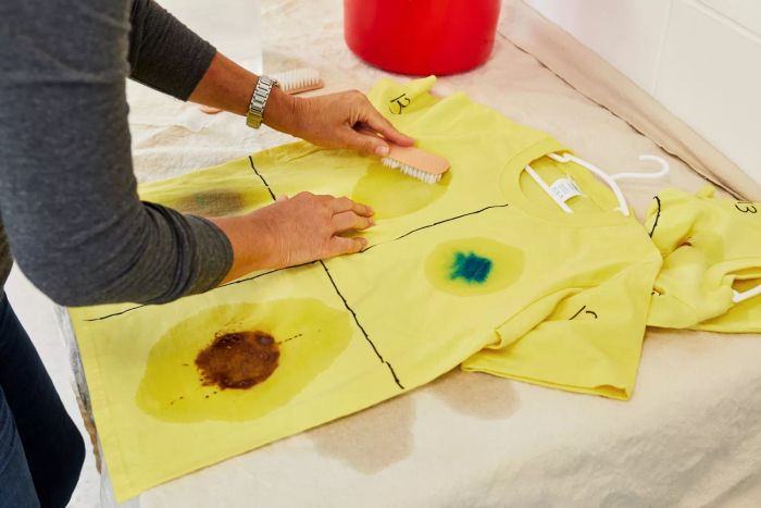 A person is scrubbing a stained T-shirt using a brush to clean it.