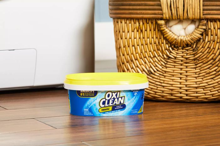 The OxiClean Versatile Stain Remover Powder on a wooden floor, placed next to a basket.