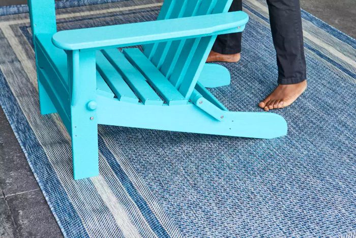 A person placing a blue Adirondack chair on the Unique Loom Outdoor Collection Transitional Indoor/Outdoor Area Rug