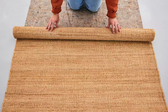 A person rolling up the Revival Hart Jute Rug