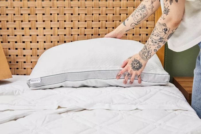 An individual places the Coop The EdenCool+ Adjustable Pillow on a bed