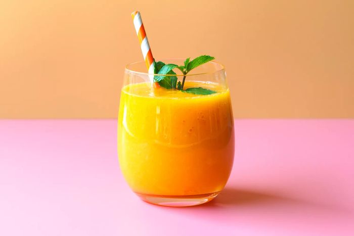 A refreshing mango smoothie garnished with mint leaves, set against a vibrant orange and pink background, perfect for a summer fruit drink concept.